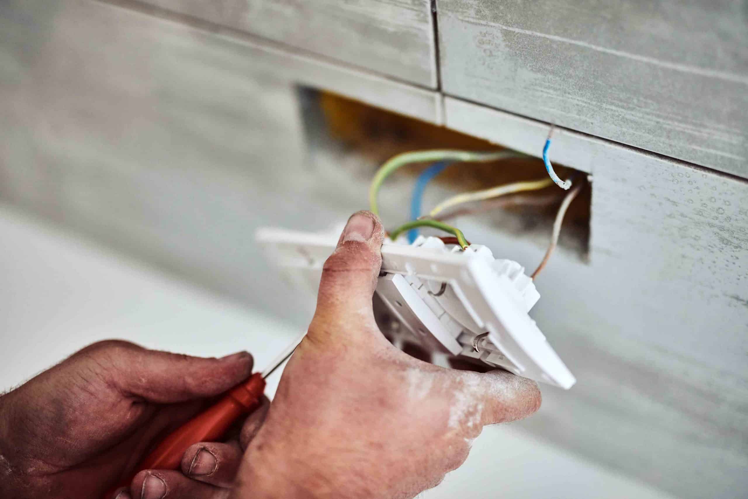 Person montiert elektrische Steckdose mit Schraubendreher an einer Wand.