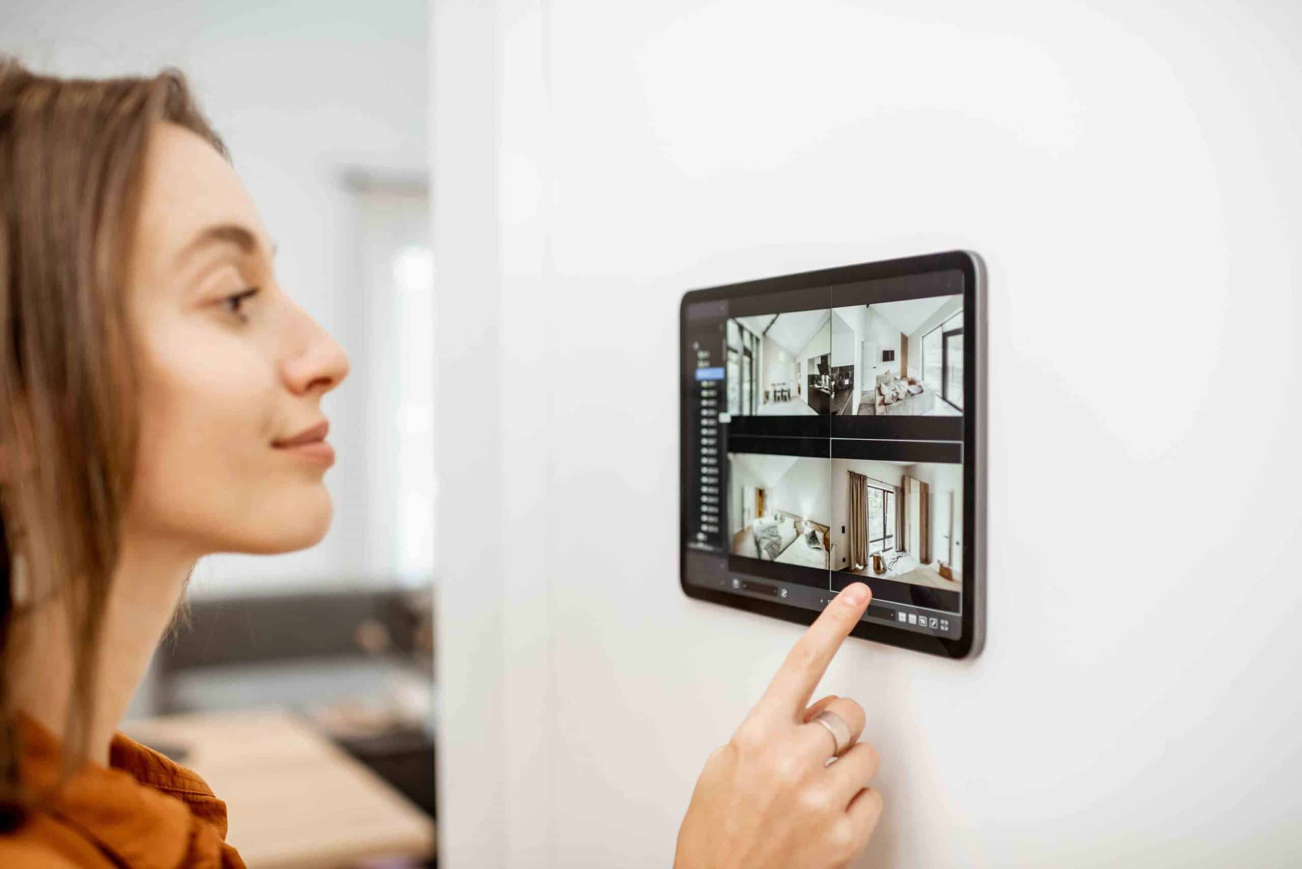 Frau bedient wandmontiertes Tablet mit Bildern verschiedener Innenräume.