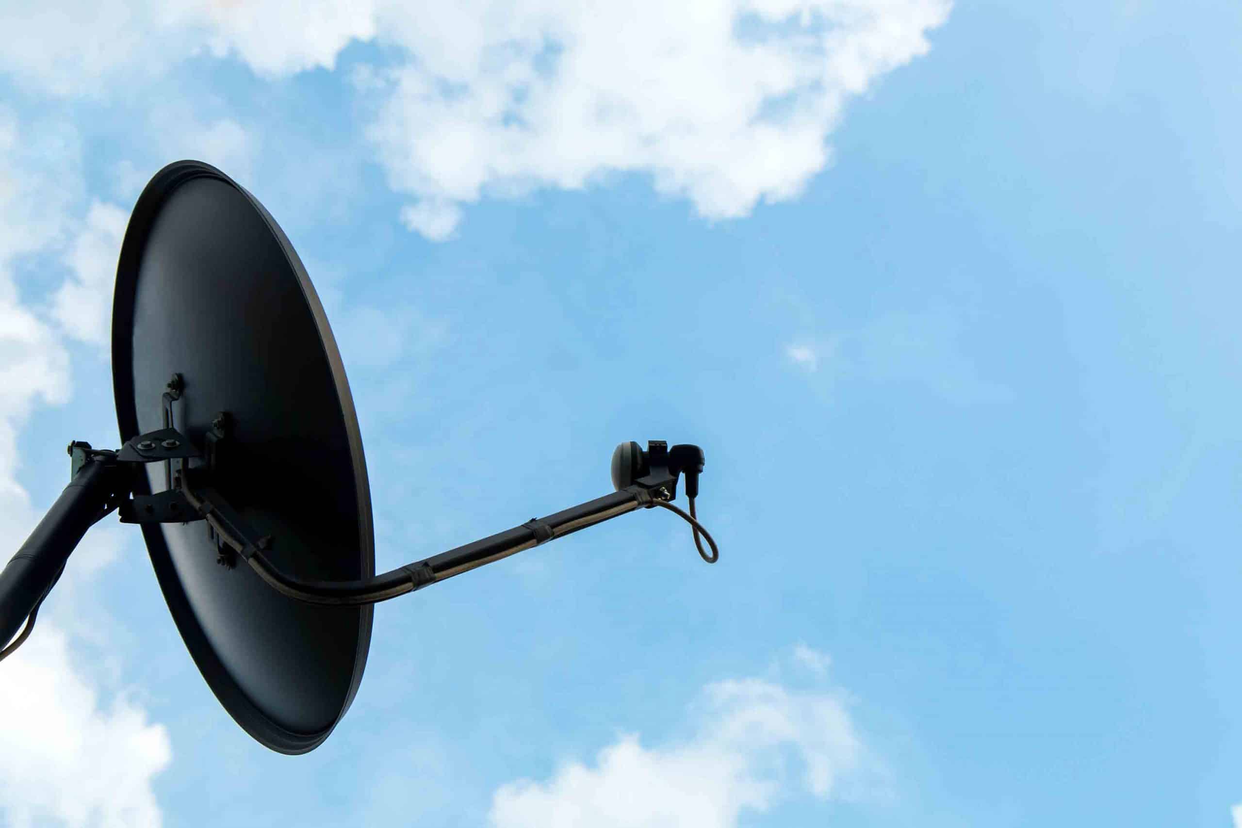 Schwarze Satellitenschüssel vor blauem Himmel mit einzelnen weißen Wolken.