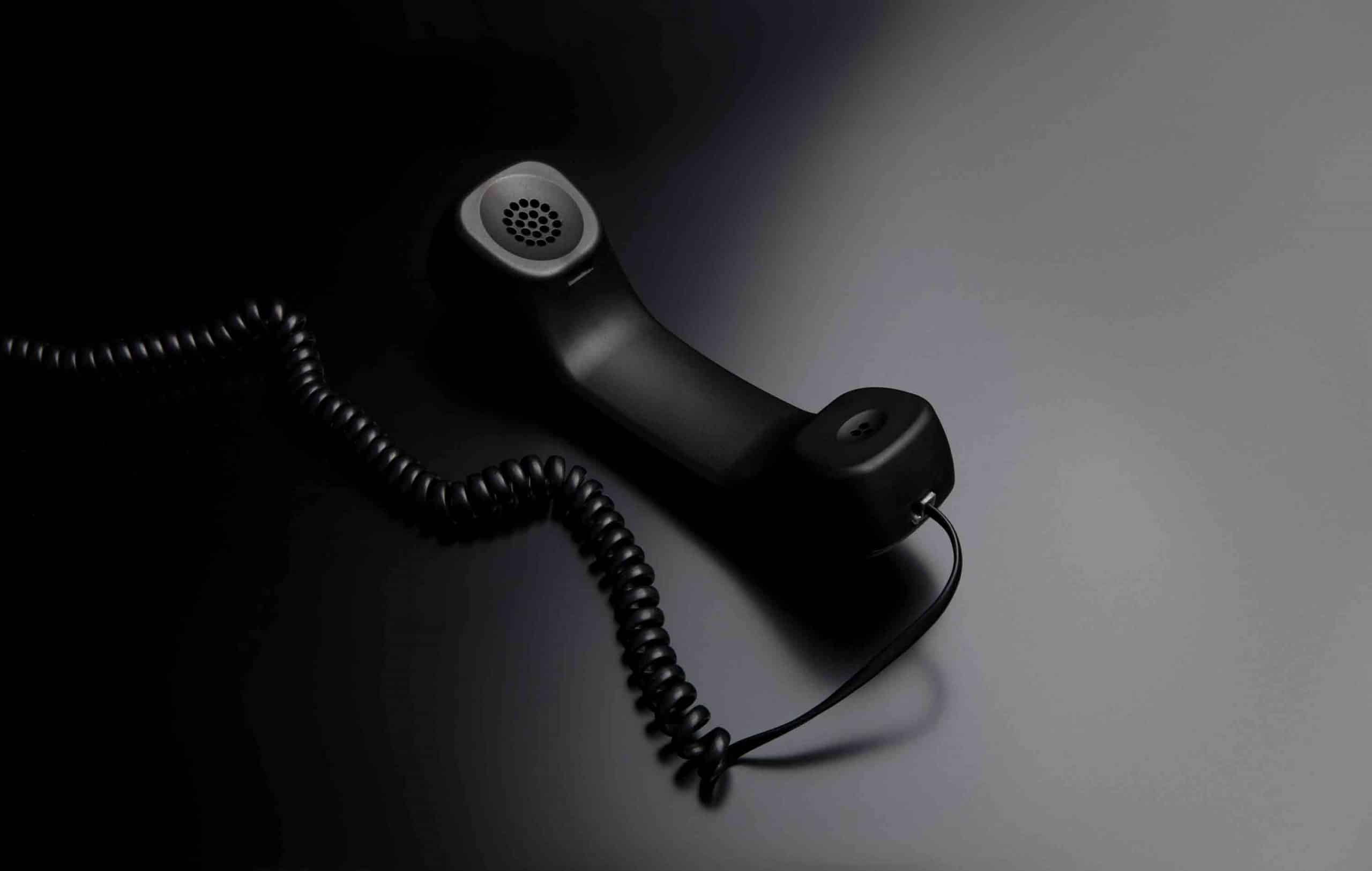 Schwarzer Telefonhörer mit Spiralkabel auf beleuchteter Oberfläche, rechter Bereich hell, links dunkel.