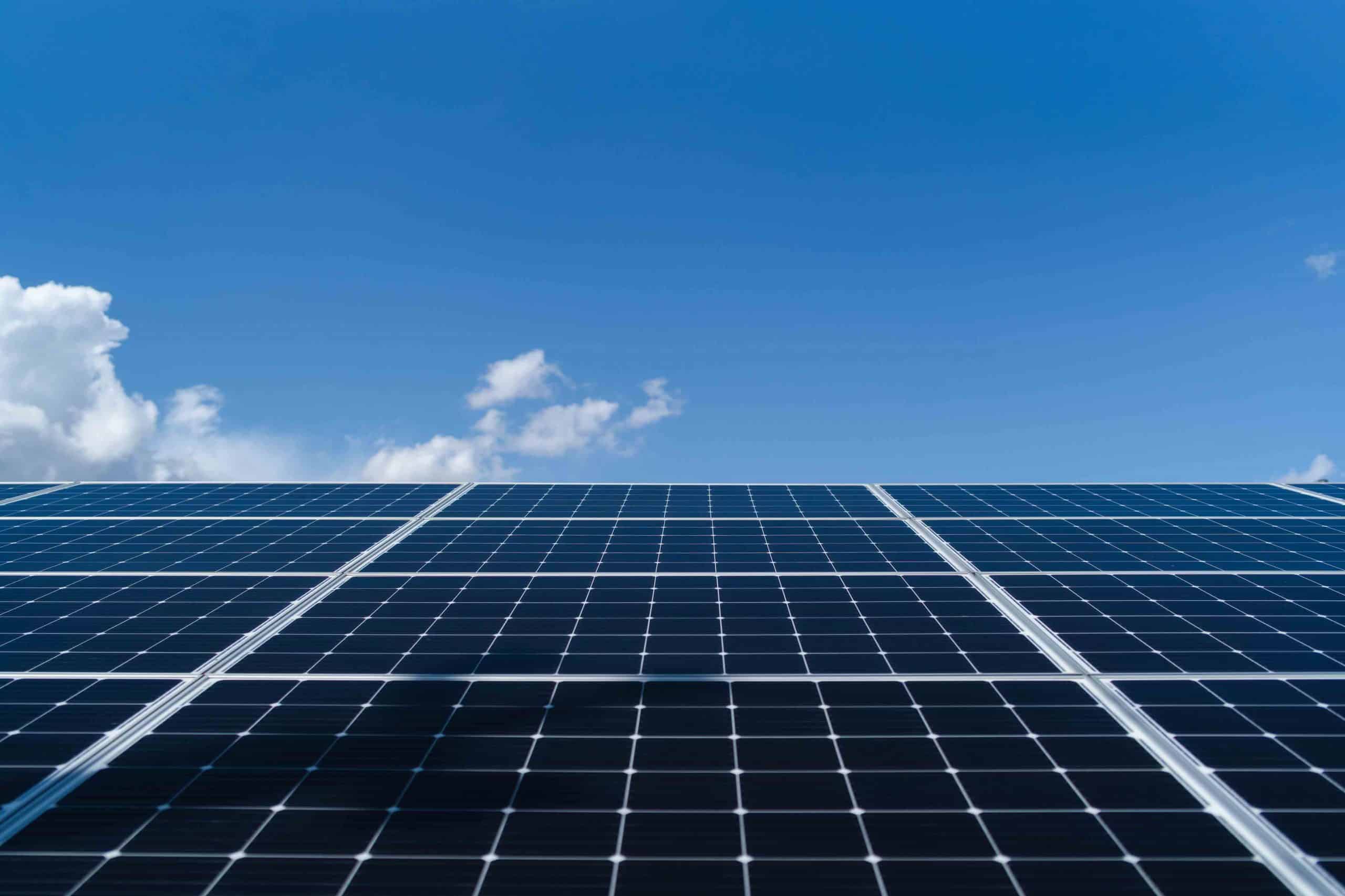 Solarmodule vor klarem, blauem Himmel mit vereinzelten Wolken.