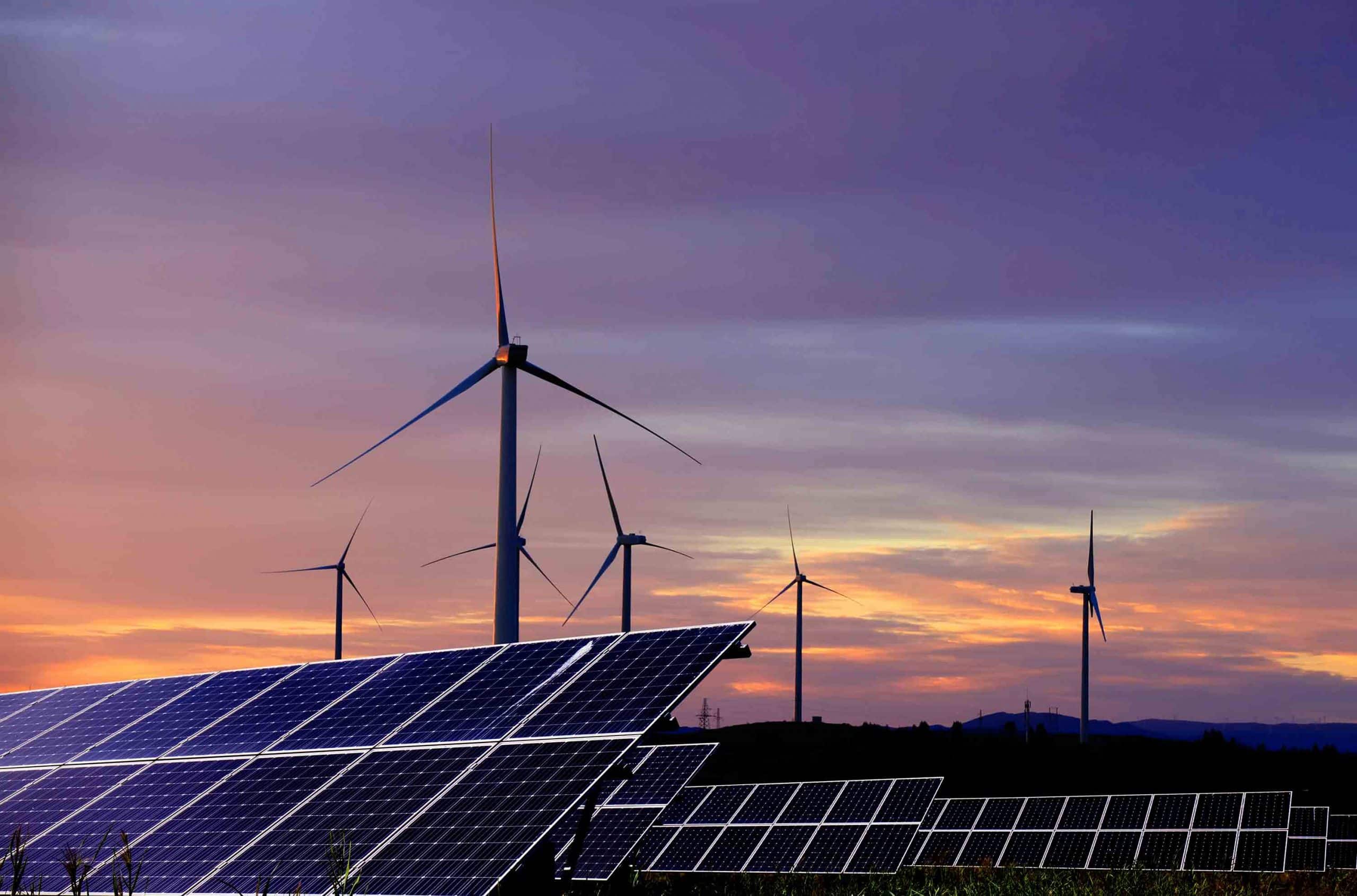 Solarpanels im Vordergrund und Windkraftanlagen im Hintergrund bei Sonnenuntergang.